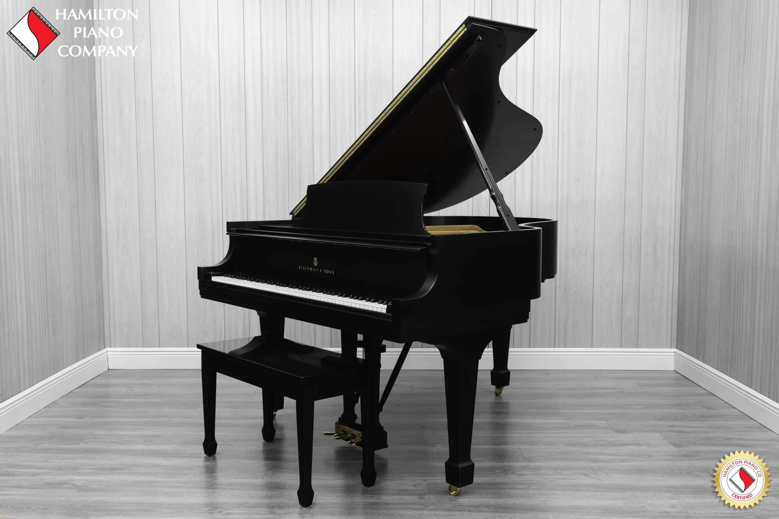 A Steinway M baby grand piano in a beautiful satin ebony finish with brass hardware and a bench.