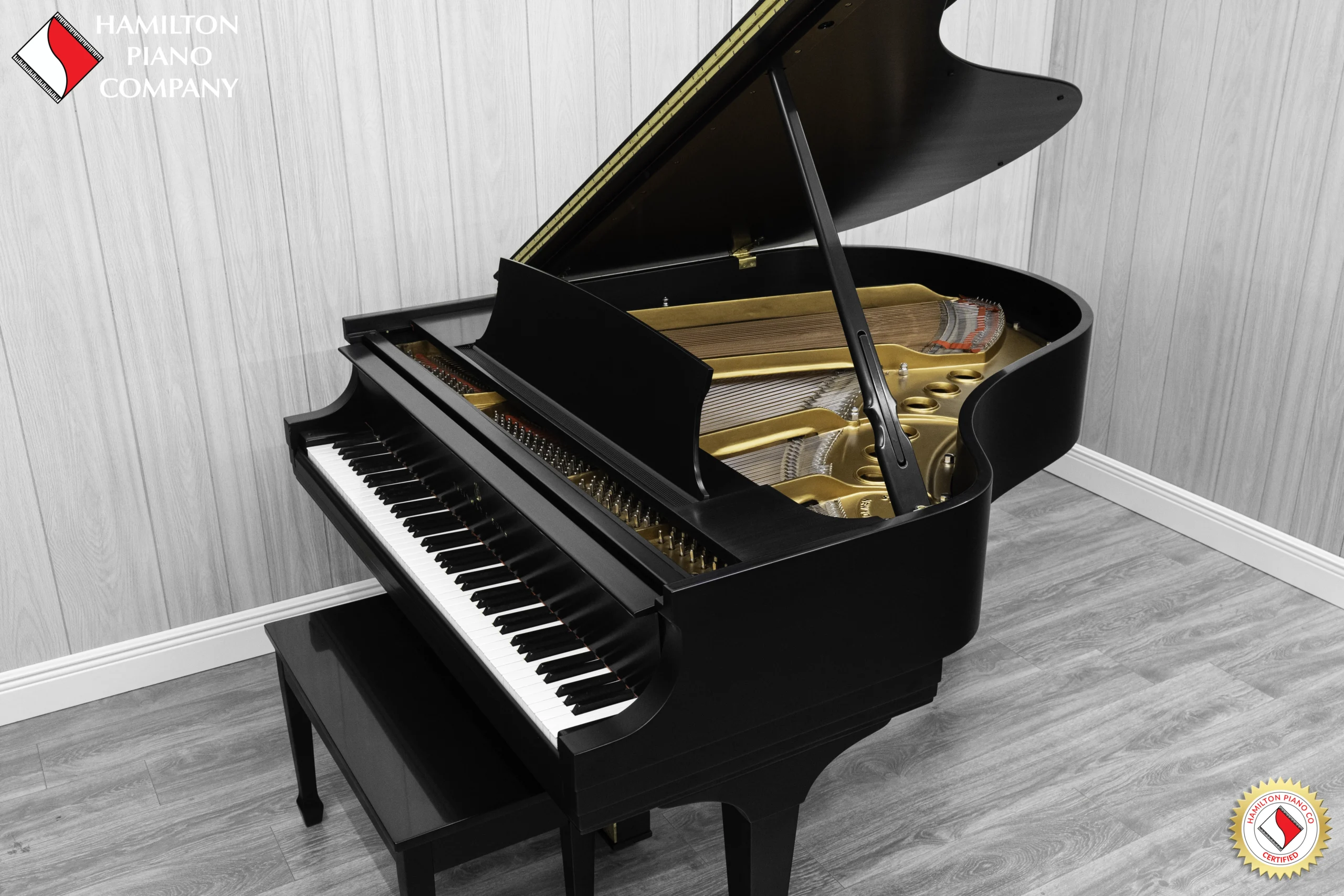 A Steinway M baby grand piano in a beautiful satin ebony finish with brass hardware and a bench. The image shows off the interior of the piano including the harp and strings.