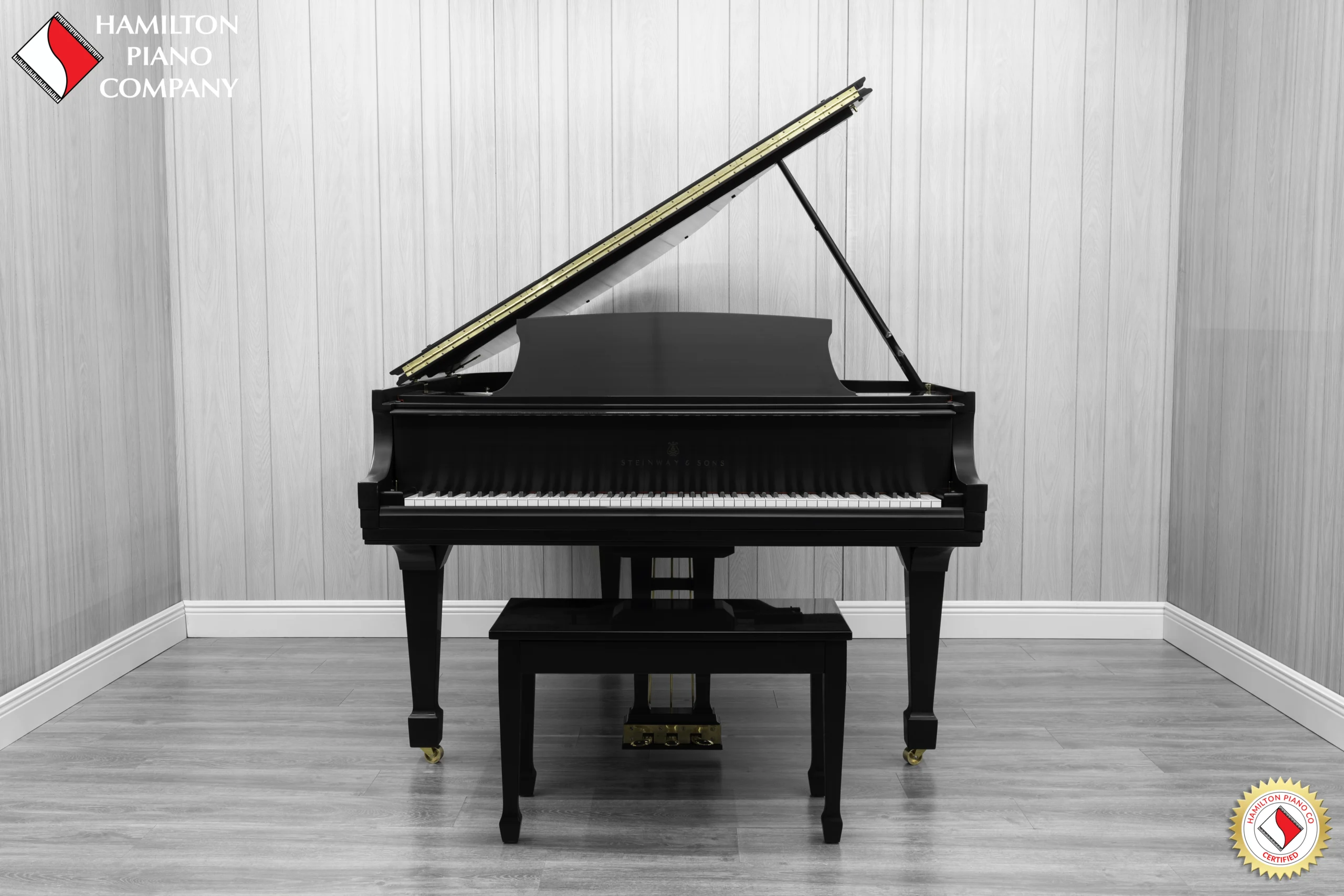 A Steinway M baby grand piano in a beautiful satin ebony finish with brass hardware and a bench.