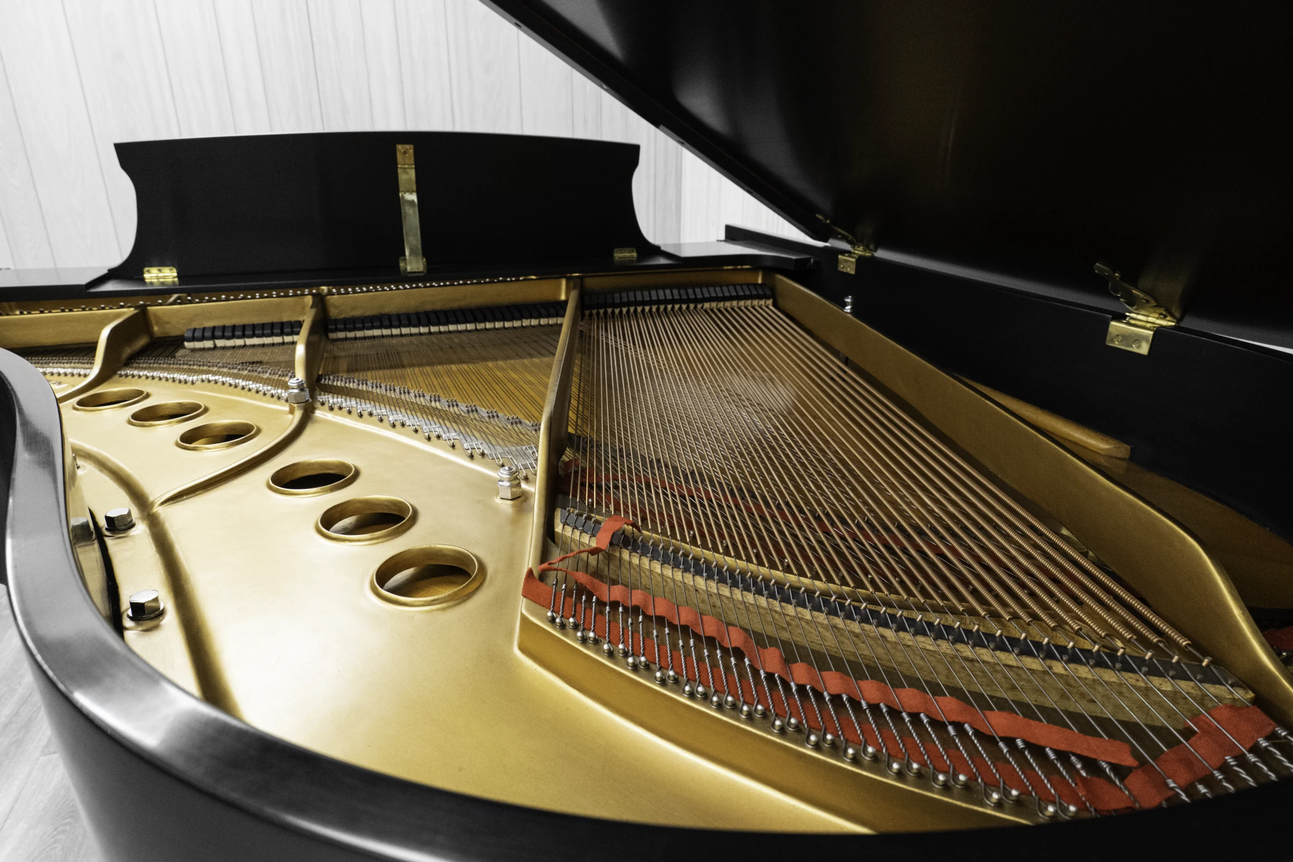 A Steinway M baby grand piano in a beautiful satin ebony finish with brass hardware and a bench. The image shows off the interior of the piano including the harp and strings.