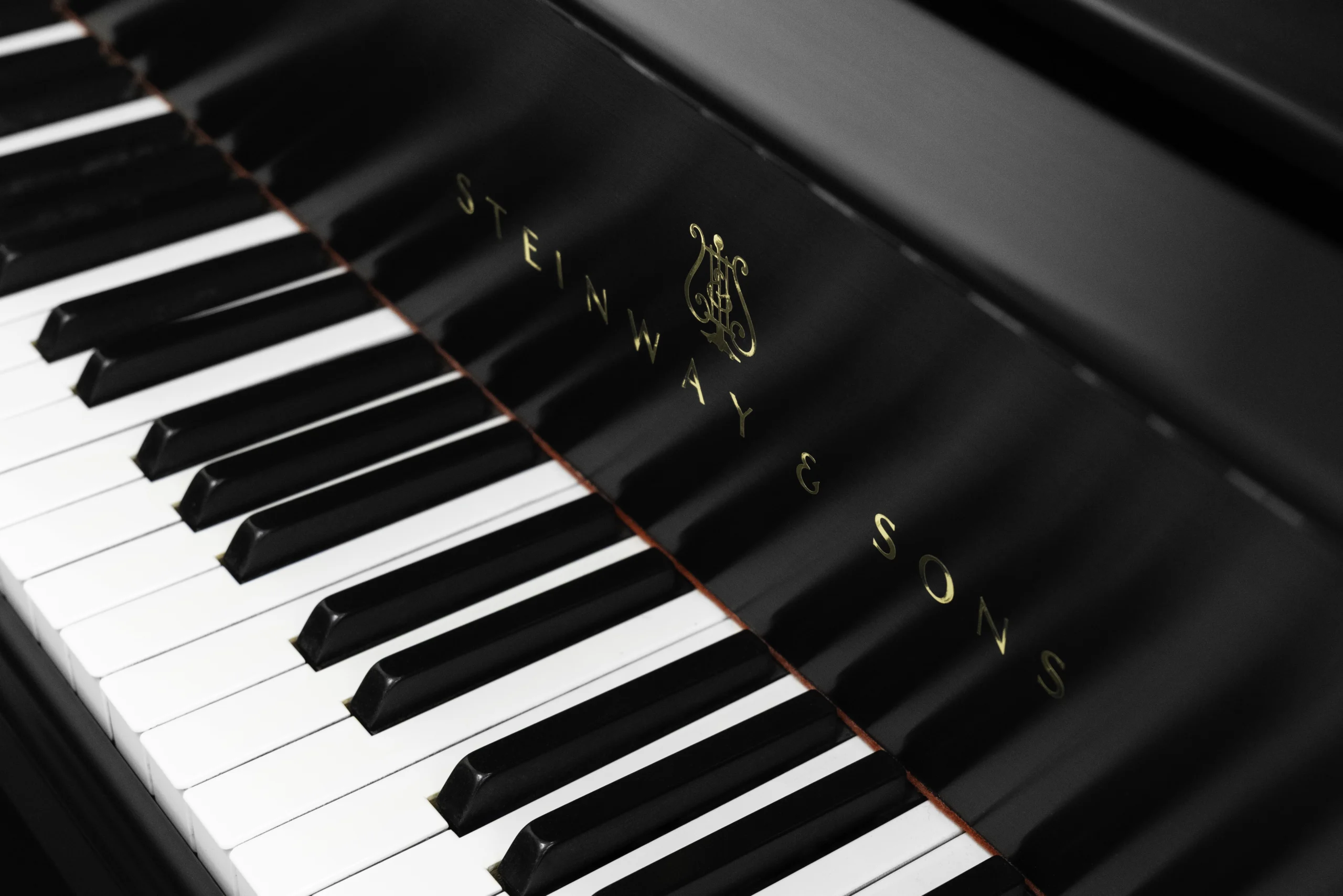 A Steinway M baby grand piano in a beautiful satin ebony finish. The image shows off the keys and Steinway logo.