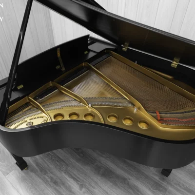 A Steinway M baby grand piano in a beautiful satin ebony finish with brass hardware and a bench. The image shows off the interior of the piano including the harp and strings.