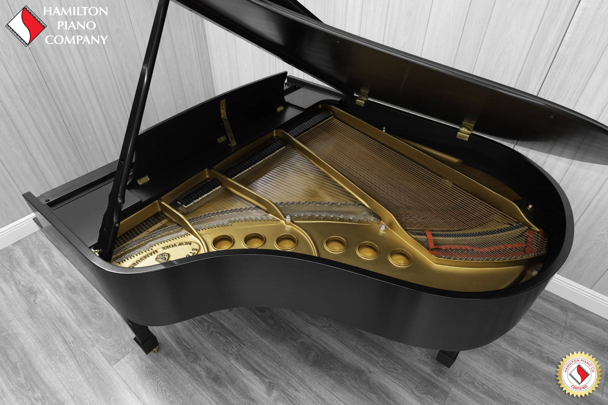 A Steinway M baby grand piano in a beautiful satin ebony finish with brass hardware and a bench. The image shows off the interior of the piano including the harp and strings.