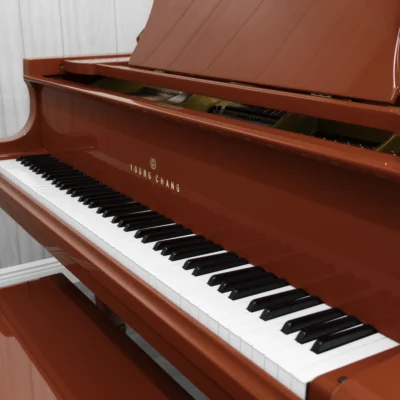 A Young Chang G-157 baby grand piano in a high polish red finish with matching bench. This image shows off the keys and Young Chang logo on the fallboard.