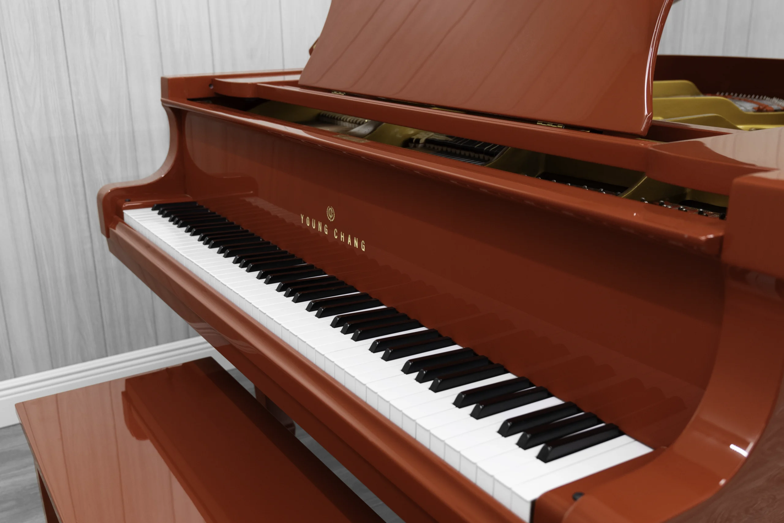 A Young Chang G-157 baby grand piano in a high polish red finish with matching bench. This image shows off the keys and Young Chang logo on the fallboard.