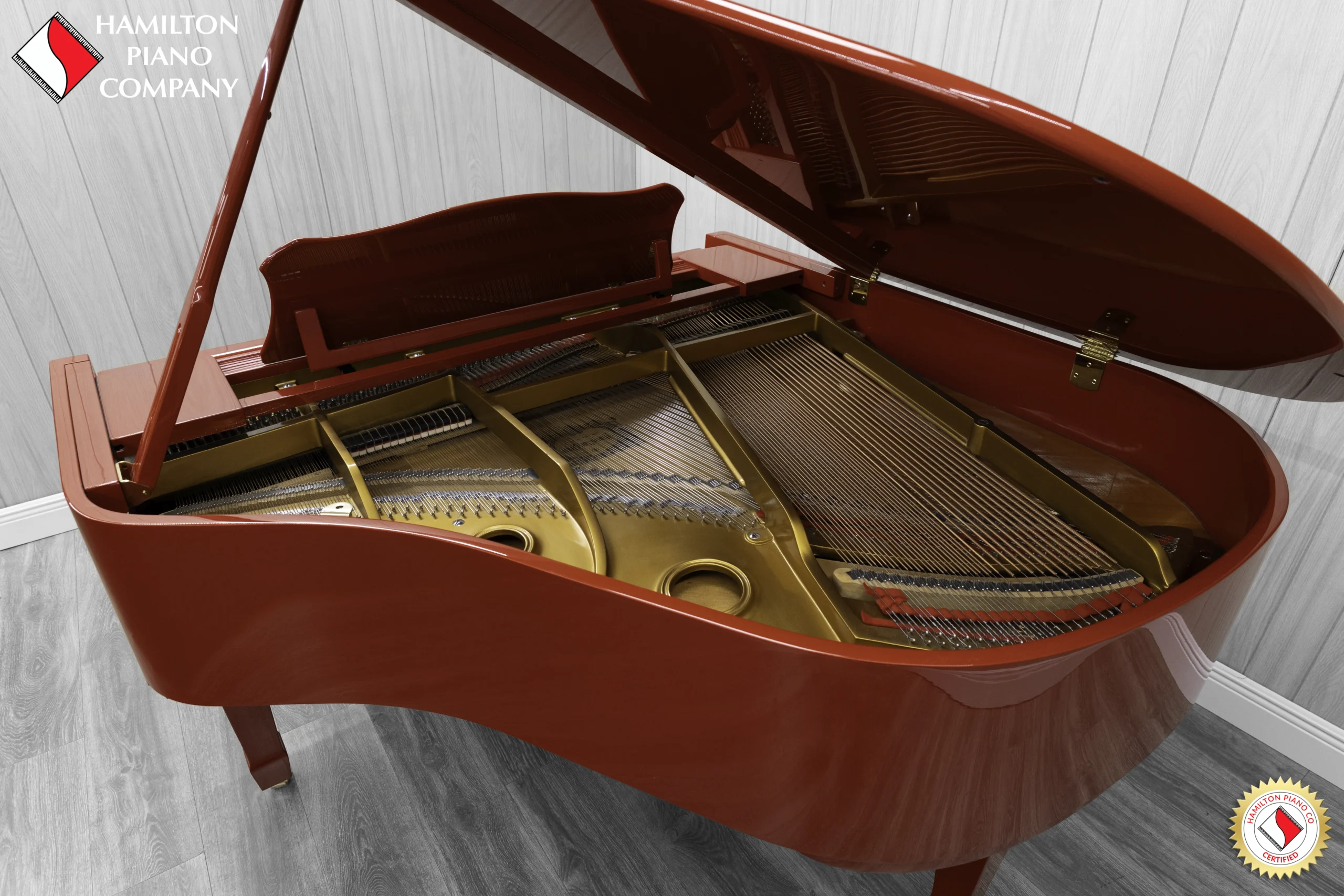 A Young Chang G-157 baby grand piano in a high polish red finish with matching bench. This image shows off the interior of the piano, including the harp and strings.