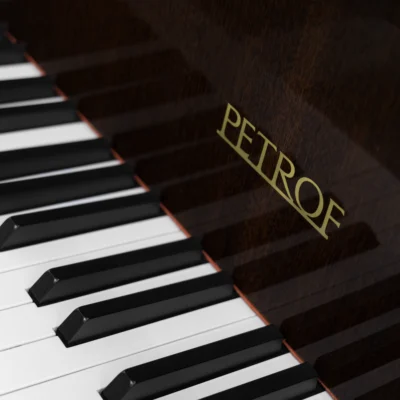 image of a Petrof baby grand piano in high polish mahogany finish focusing on the keys and fallboard logo