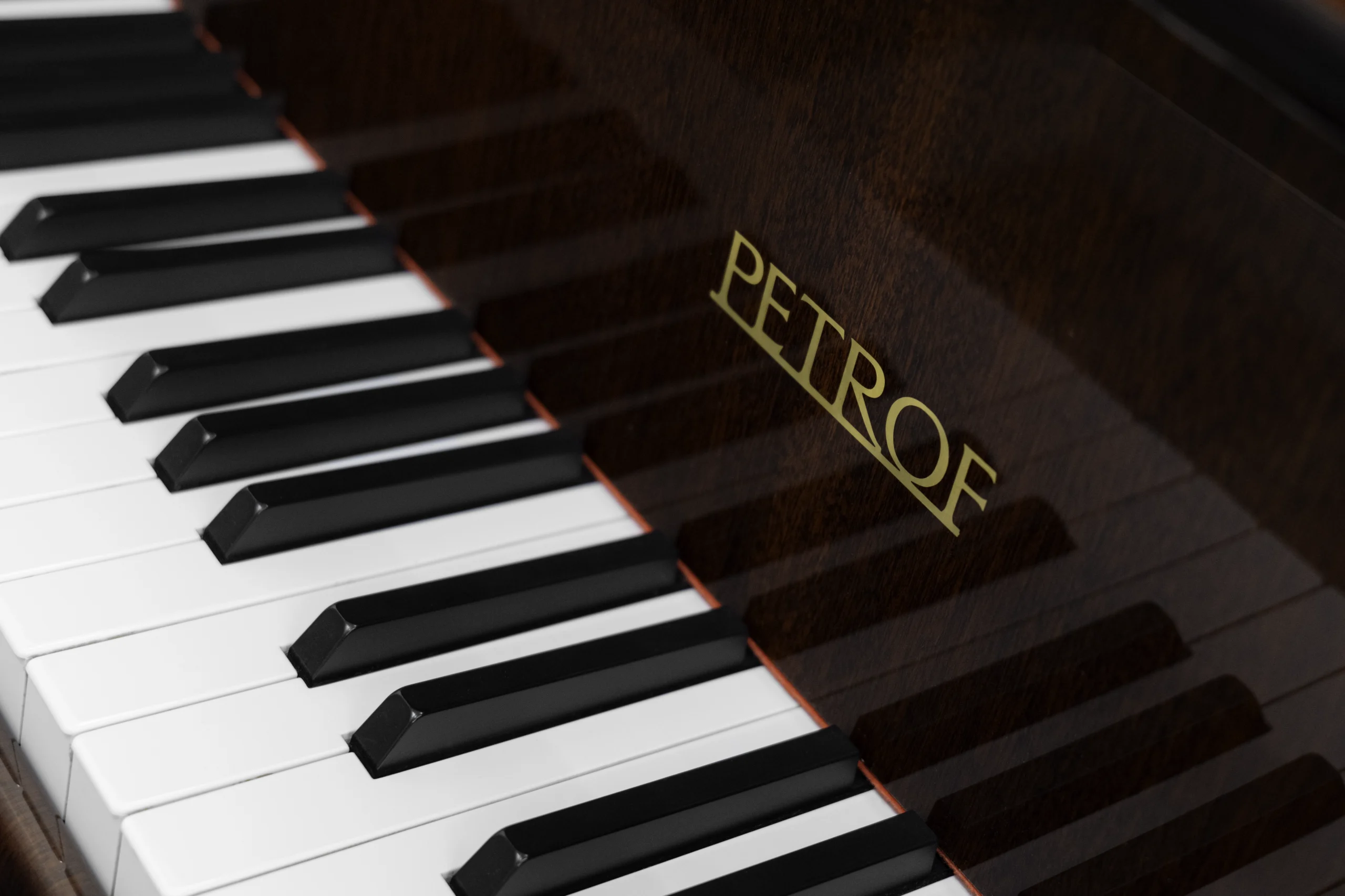 image of a Petrof baby grand piano in high polish mahogany finish focusing on the keys and fallboard logo